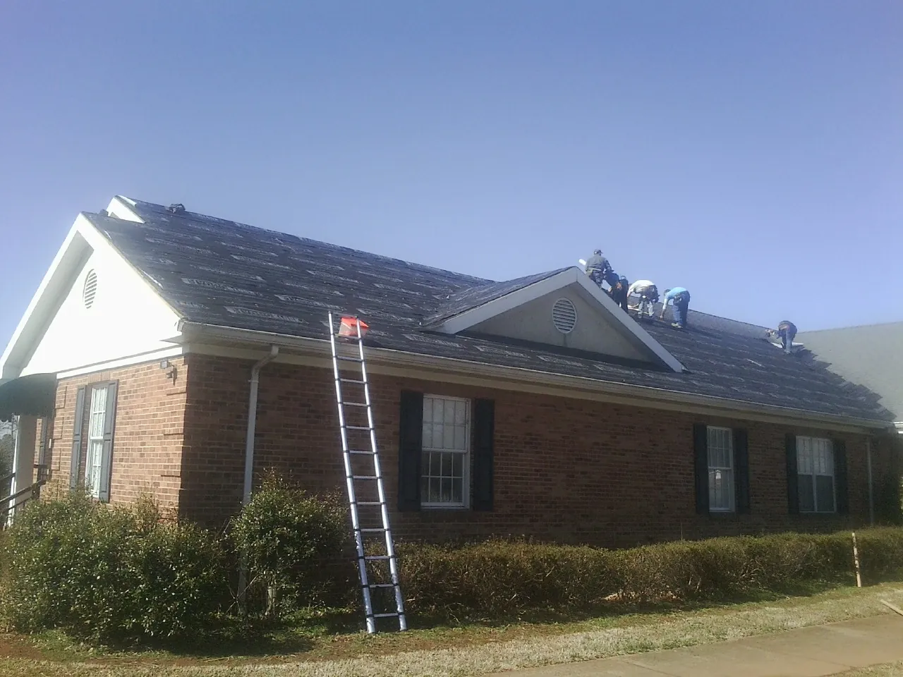 Crew tearing shingles off a brick ranch roof with a ladder set — Metal Roof Repair work by our crew in Rootstown