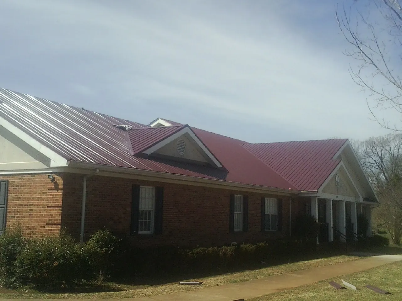 Red metal roof with gabled entries on a long brick building, from a Hail Damage Roof Repair job in Rootstown