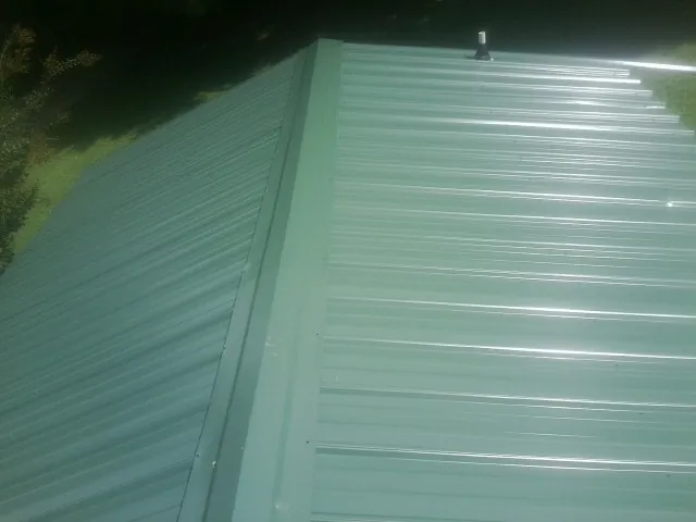 New green metal panels meeting at the ridge of a roof — Flat Roof Repair work by our crew in Rootstown