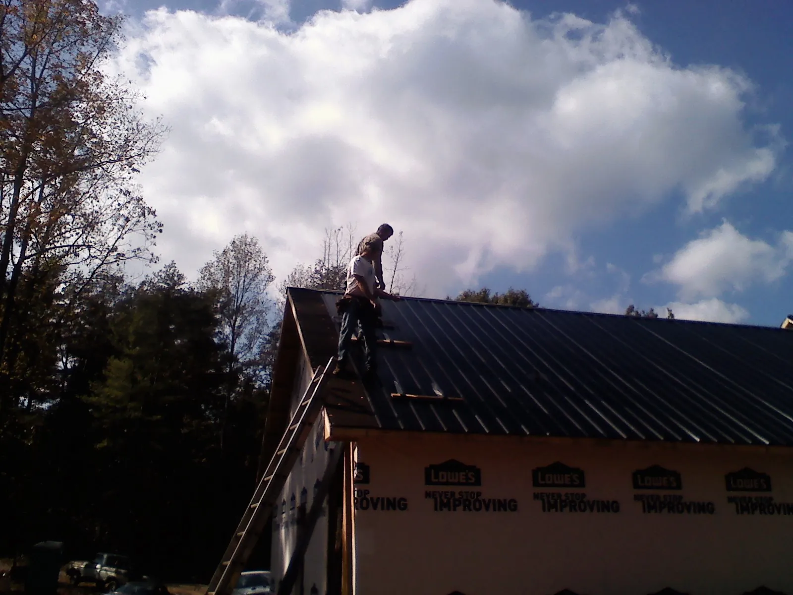 Roofer fastening dark metal panels high against a cloudy sky, from a Roof Inspection job in Rootstown